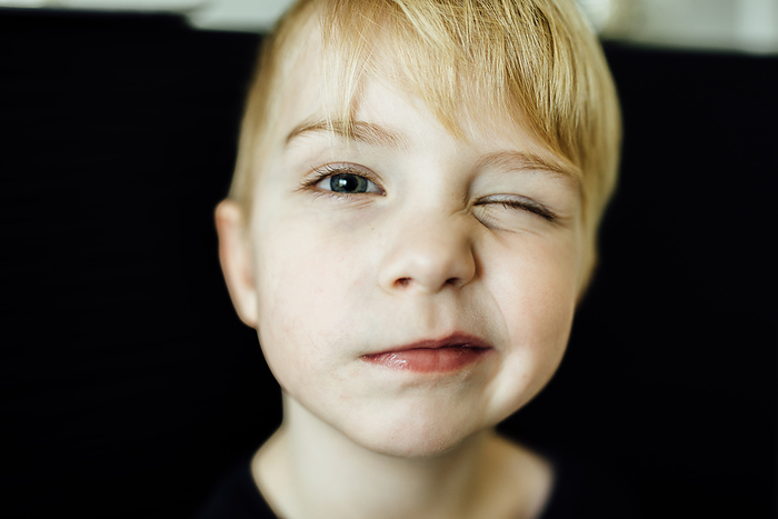 Young boy winks with goofy face at camera with black background, by Cavan Images / Kimberli Fredericks