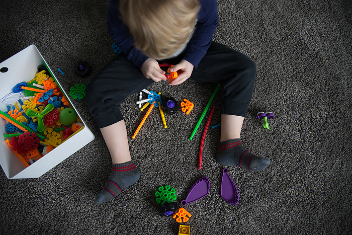 Overhead view of boy playing with building materials on carpeted, by Cavan Images / Kimberli Fredericks