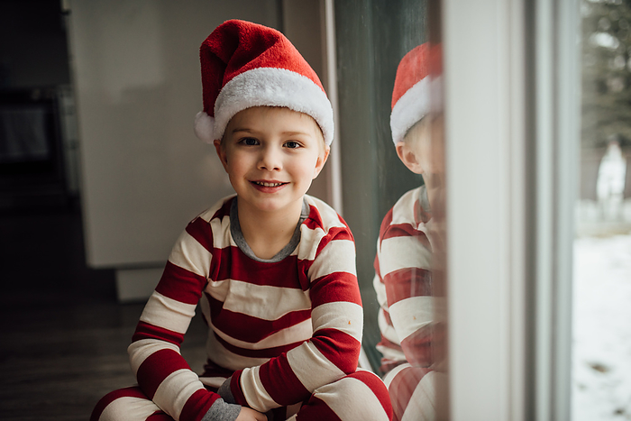 Little boy looks at camera and smiles while wearing Christmas pa, by Cavan Images / Kimberli Fredericks