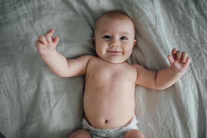 Overhead shot of baby boy in diaper smiling happily and reaching, by Cavan Images / Kimberli Fredericks
