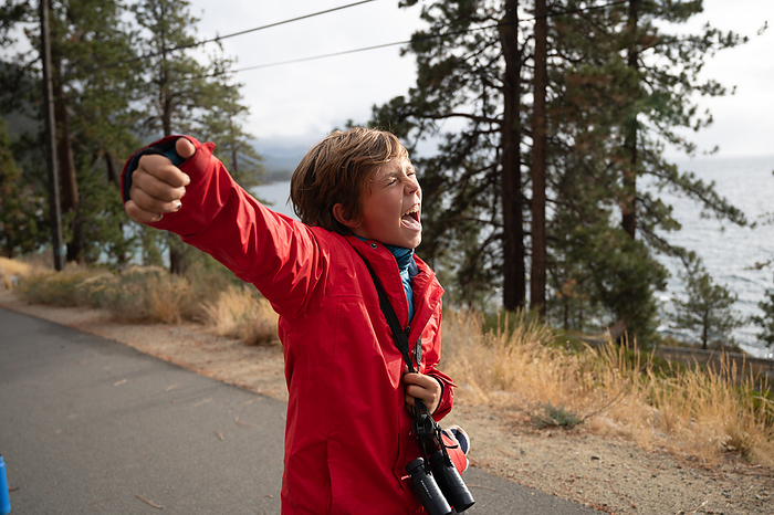 Joyful tween in red raincoat with fist lifted on a trail near lake, by Cavan Images / Liz Celeste