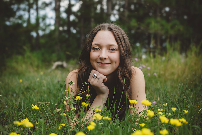 Young smiling teen girl laying in flower field senior picture, by Cavan Images / Melissa Clemons