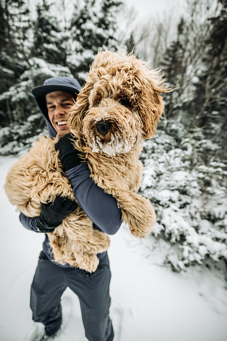 Smiling young man holds his snow covered dog while walking in NH, by Cavan Images / Chris Bennett