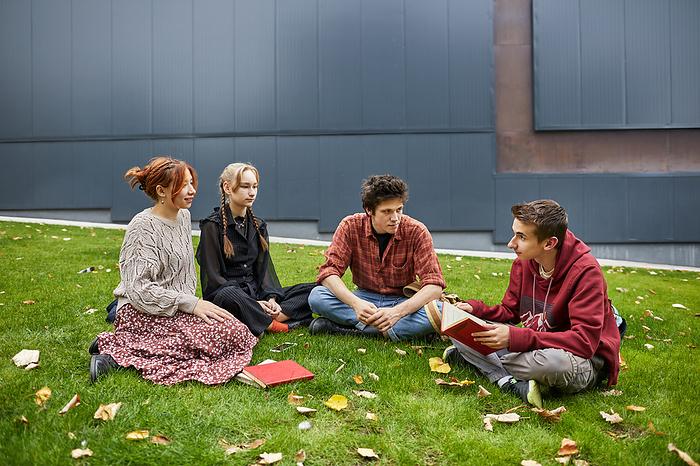 students reading a book in the campus courtyard, by Cavan Images / Elena Perevalova