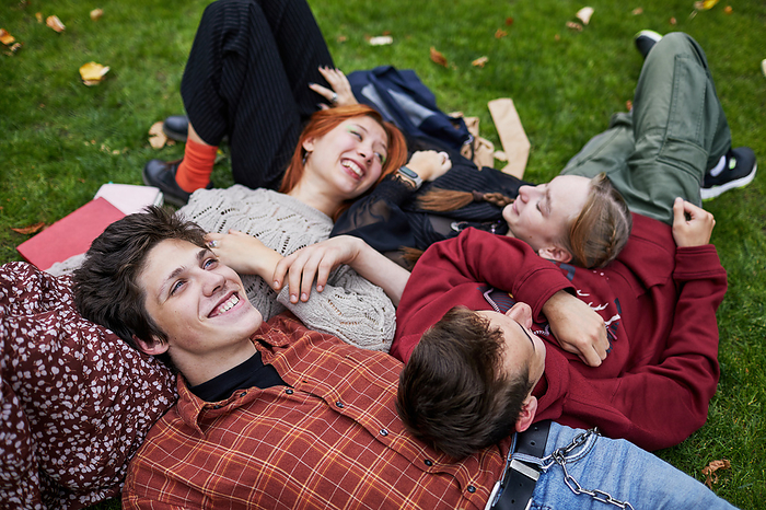 laughing friends lying on the grass, by Cavan Images / Elena Perevalova