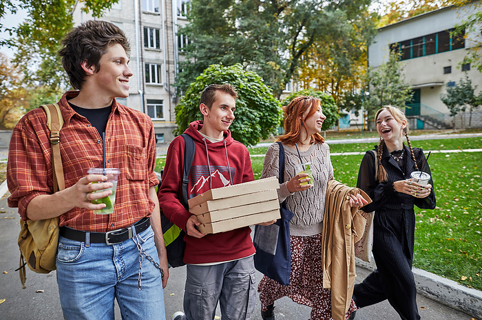 happy young people walking with pizza and drinks on the street, by Cavan Images / Elena Perevalova