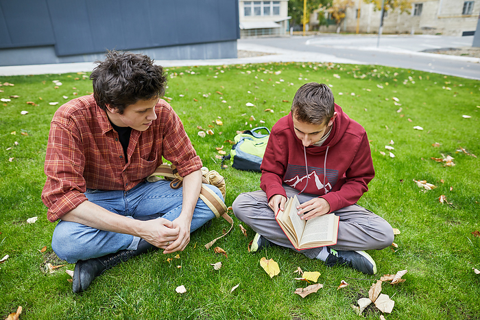 guys looking at a book in the school yard, by Cavan Images / Elena Perevalova