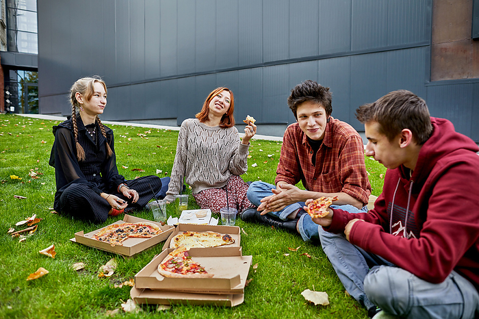 group of friends eating pizza and laughing on the lawn, by Cavan Images / Elena Perevalova