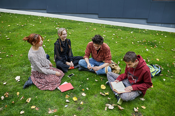 group of students reading  book on the lawn in the campus courtyard, by Cavan Images / Elena Perevalova