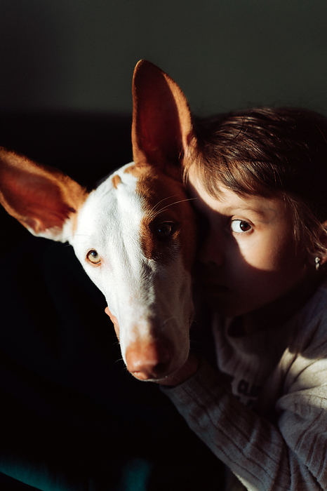 Friendship between children and dogs, girls hugging a dog., by Cavan Images / Yuliya Kirayonak