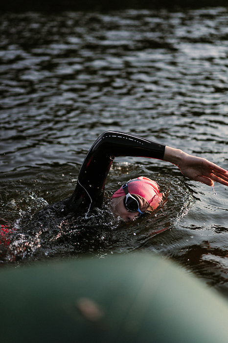 Professional swimmer in a wetsuit swims in open water on a lake., by Cavan Images / Yuliya Kirayonak