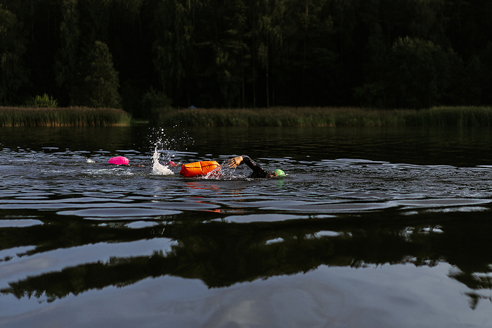 Professional swimmer in a wetsuit swims in open water on a lake., by Cavan Images / Yuliya Kirayonak