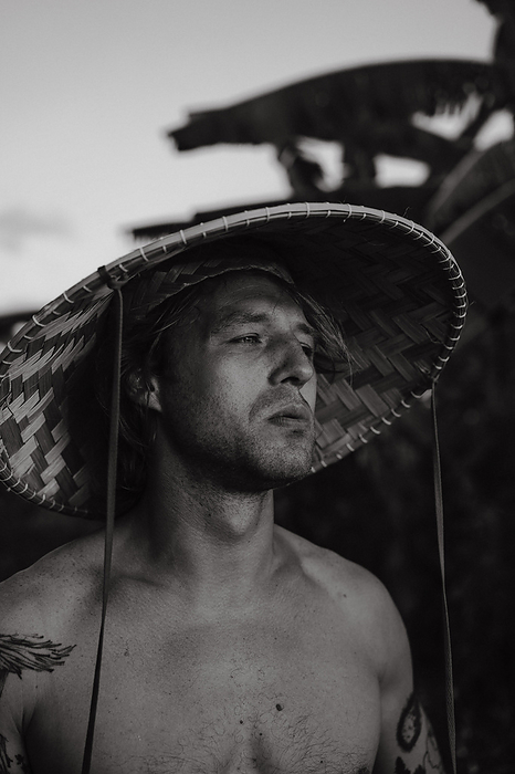 A young man wearing an Asian cone hat in rice fields at sunset. Bali., by Cavan Images / Yuliya Kirayonak