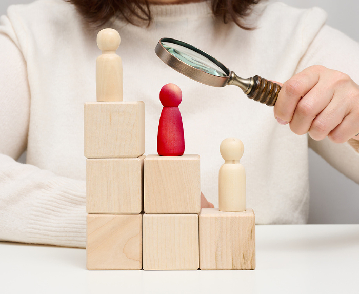 Woman holding a magnifying glass and wooden men on a white table. Personnel recruitment concept, talented employees. Career advancement Woman holding a magnifying glass and wooden men on a white table. Personnel recruitment concept, talented employees. Career advancement