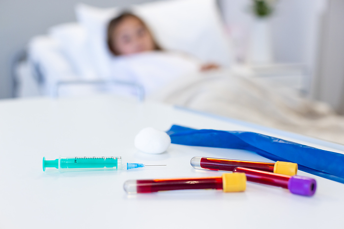 Syringe and blood samples on table, caucasian girl patient in hospital bed in background, copy space. Diagnosis, blood test, childhood, illness, medical services, healthcare and hospital, unaltered.