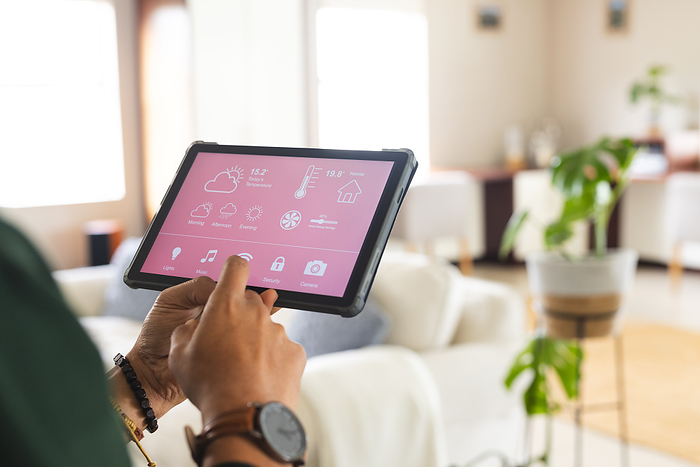 Biracial man with wristwatch checking smart home controls on tablet in sunny living room at home. Lifestyle, free time and domestic life, technology, communication, unaltered.
