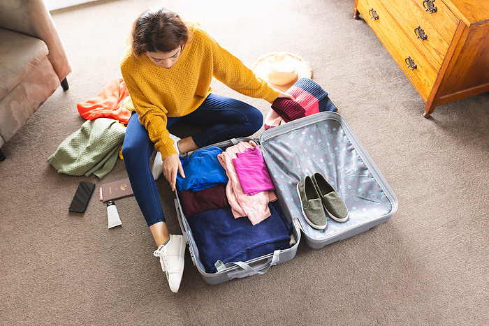 Biracial woman packing suitcase on floor at home. Lifestyle, travel, vacation and domestic life, unaltered.