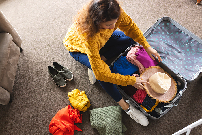 Biracial woman packing suitcase on floor at home. Lifestyle, travel, vacation and domestic life, unaltered.
