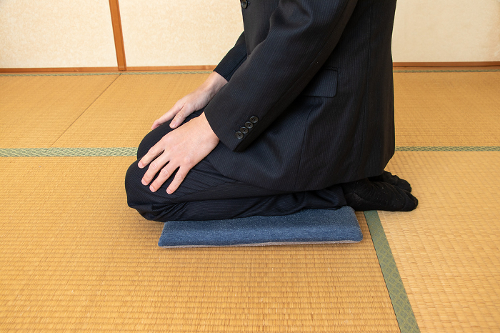 Man in black suit sitting seiza on cushion