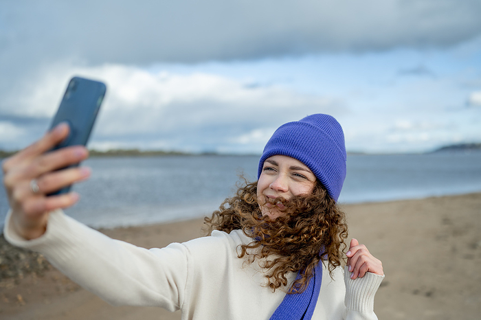 Smiling woman wearing knit hat taking selfie at beach