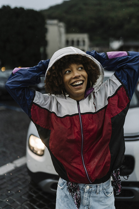 Happy young woman wearing hooded jacket in rain
