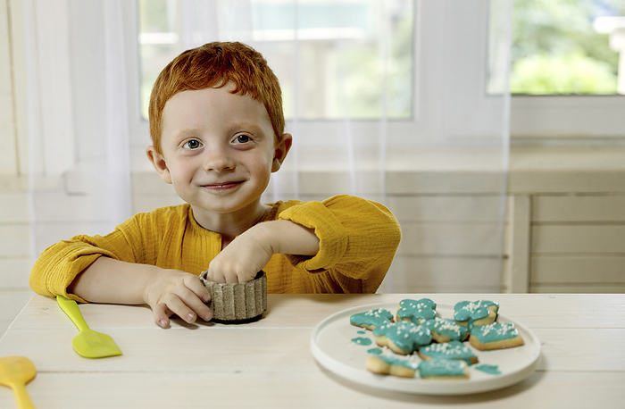 Smiling boy sitting with bowl and decorated turquoise colored cookies at table