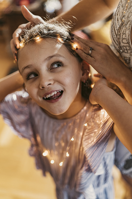 Woman adjusting string light on daughter's forehead at home