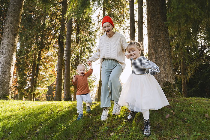 Smiling mother enjoying with children near trees in forest