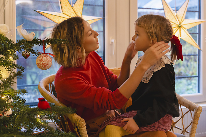 Mother talking to girl and adjusting her hair at near Christmas tree at home