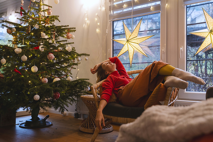 Woman relaxing on chair by Christmas tree at home