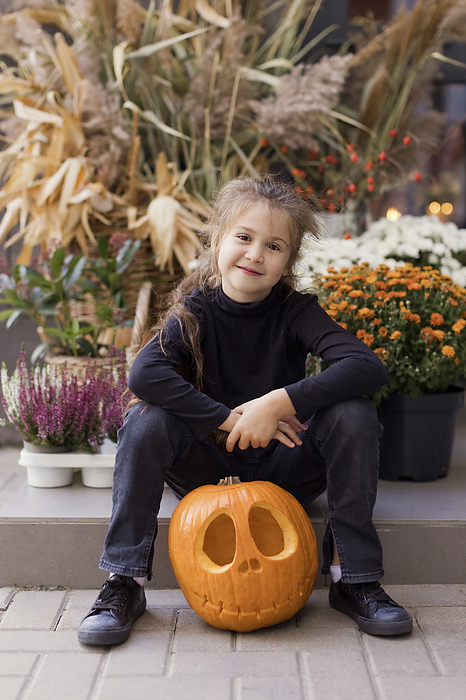 Cute girl sitting with carved pumpkin in front of plants