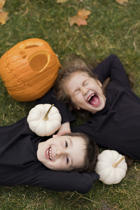 Excited siblings lying on grass with pumpkins
