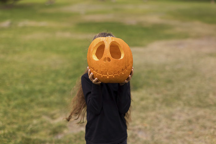 Girl covering face with carved pumpkin