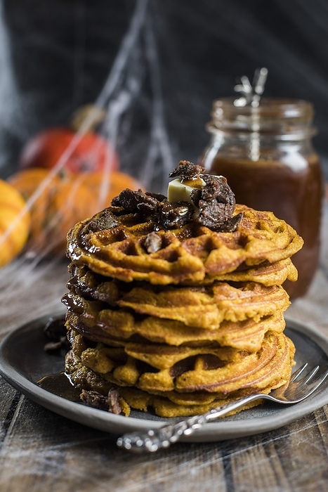 Stack of homemade pumpkin spice waffles with caramelized seeds and syrup