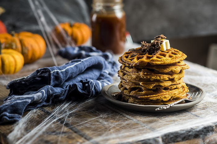Stack of homemade pumpkin spice waffles with caramelized seeds and syrup