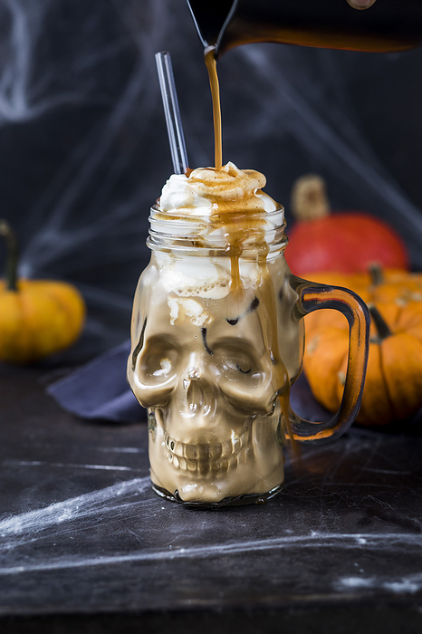 Syrup pouring on skull shaped mug of pumpkin spice latte with whipped cream