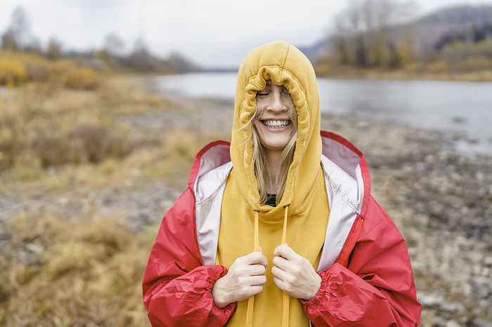 Cheerful woman tightening hooded shirt in front of river