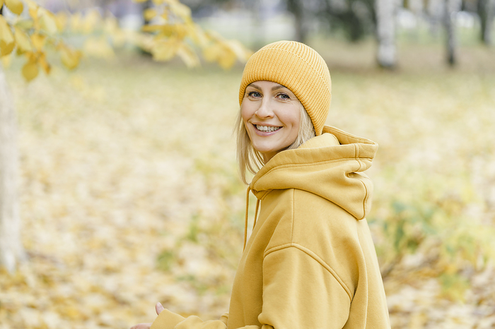 Happy woman wearing yellow hooded shirt and knit hat in park
