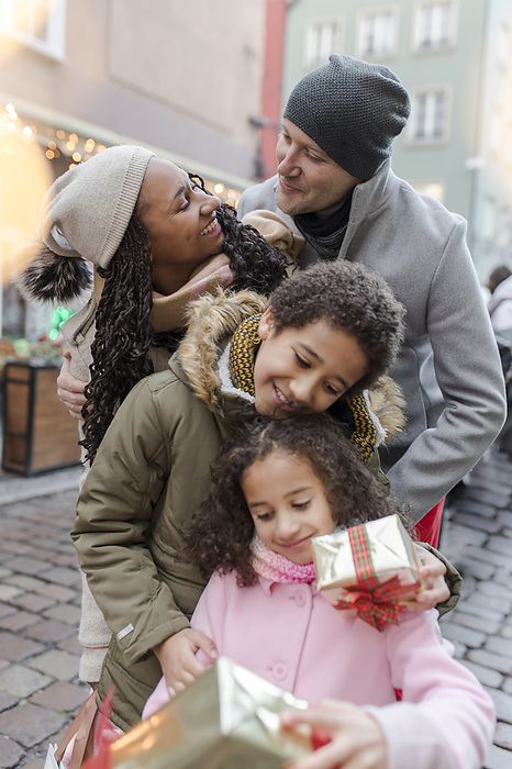 Happy parents with children holding gift boxes at Christmas market