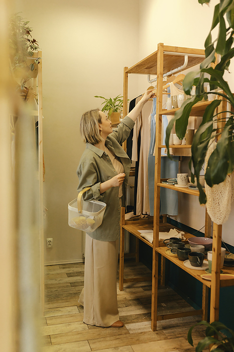 Woman with shopping basket choosing clothes in store