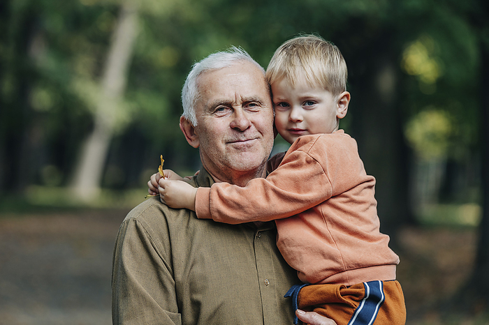 Smiling senior man carrying grandson in park