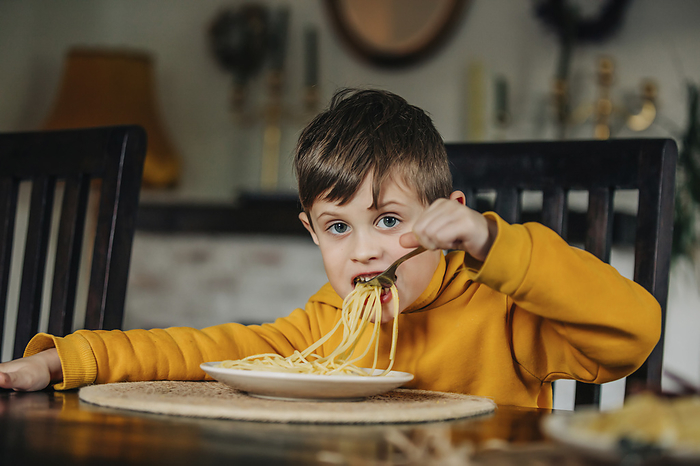 Boy wearing hooded shirt eating pasta at home