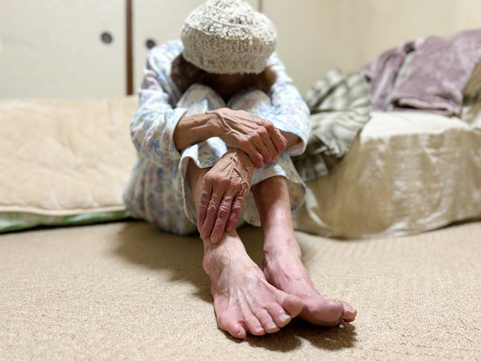 Elderly woman sitting in a nightgown in front of a futon and nodding off