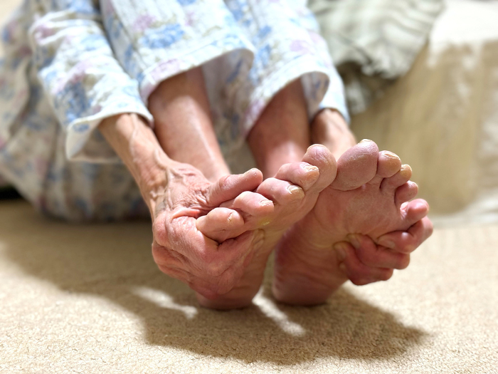 Elderly woman's hands pressing the soles of both feet in her nightgown.