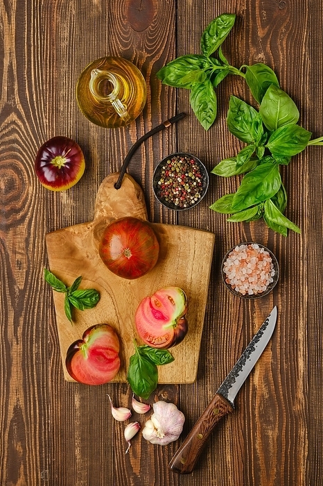 Fresh meaty tomato on wooden cutting board with basil and spice