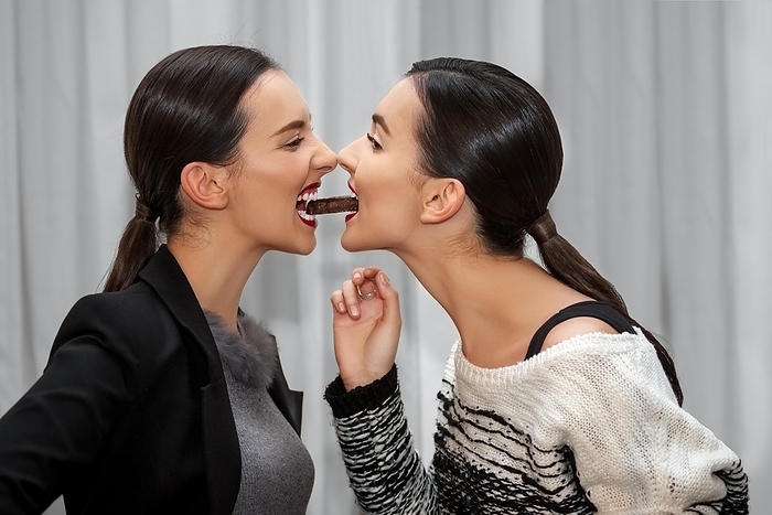Two young girls eating one sweet from mouth to mouth