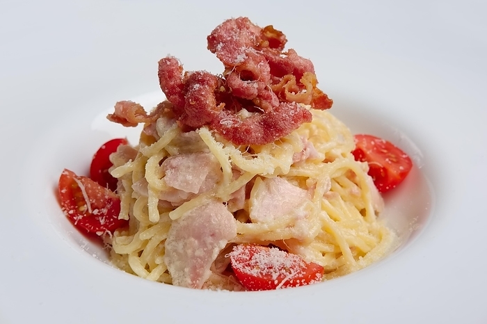 Plate with pasta served with bacon and ham, decorated with tomato cherry