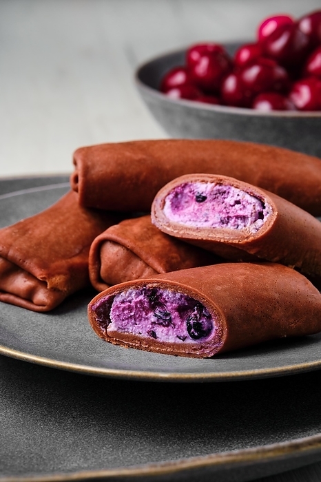 Closeup view of thin chocolate pancakes stuffed with curd, blueberry and cherry