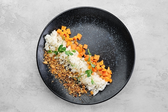 Garnish to the main dish, boiled rice, fried carrot and bread crumbs on a plate, top view
