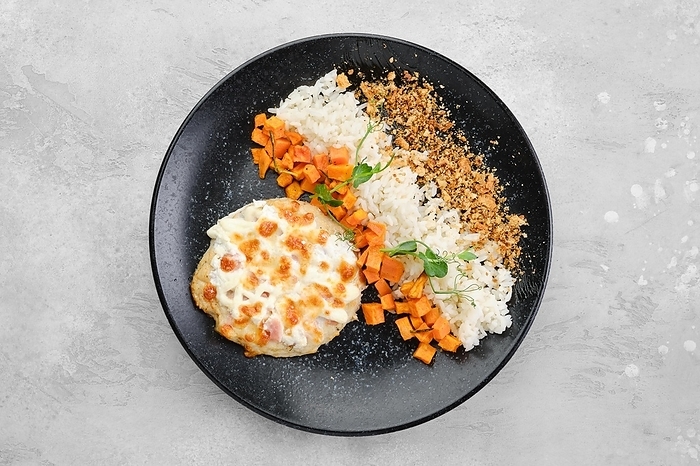 Chopped pork cutlet baked with ham and cheese served with carrot and rice on a plate, top view